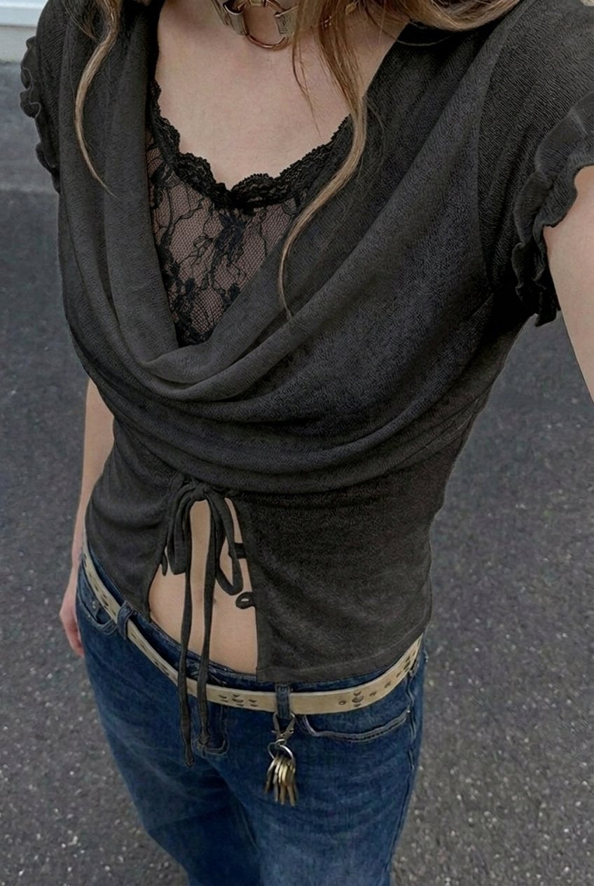Black draped cowl-neck top with scalloped-lace insert and front tie, worn with light-wash jeans — front view